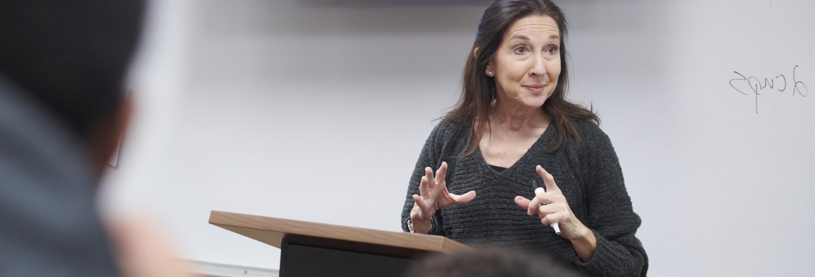 A female professor stands in front of a whiteboard